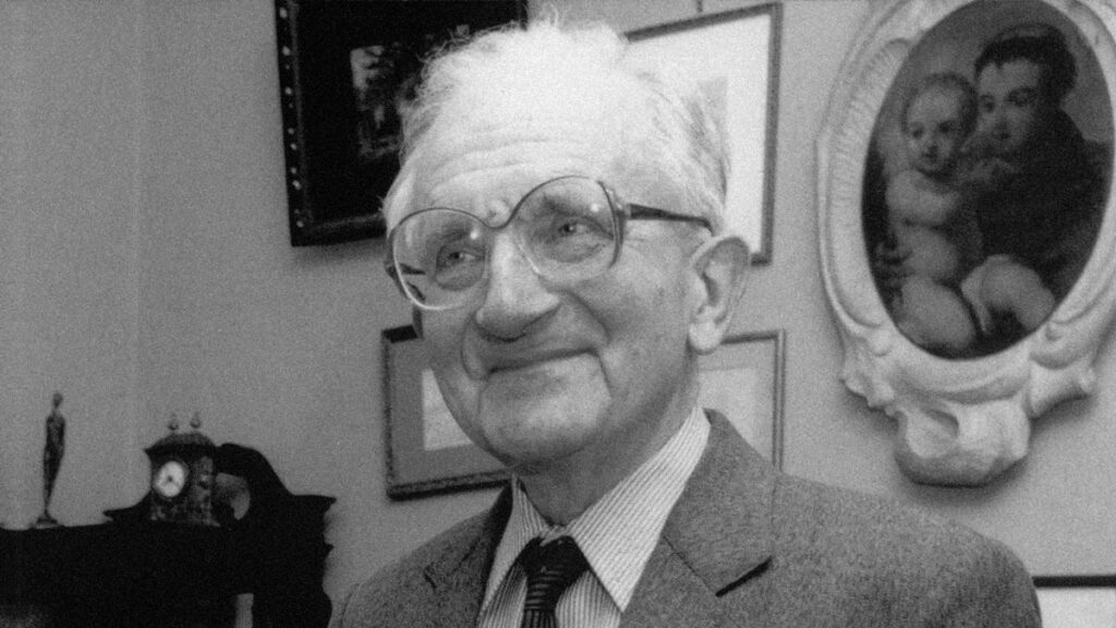 Janusz Szwalbe, mężczyzna stoi na tle obrazów.