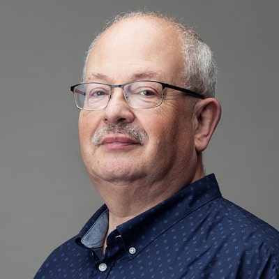 zdjęcie portretowe mężczyzny z do połowy łysą głową, siwymi włosami po bokach i owalną twarzą