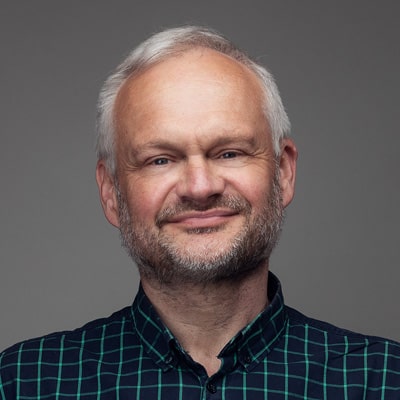 zdjęcie portretowe mężczyzny o siwych włosach, z krótkim zarostem w ciemnej koszuli w kratkę