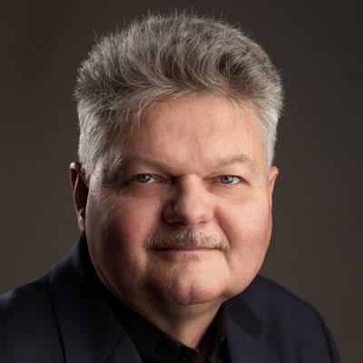 Cezary Nelkowski zdjęcie portretowe mężczyzny w średnim wieku, ze szpakowatymi bujnymi włosami i z małym wąsikiem