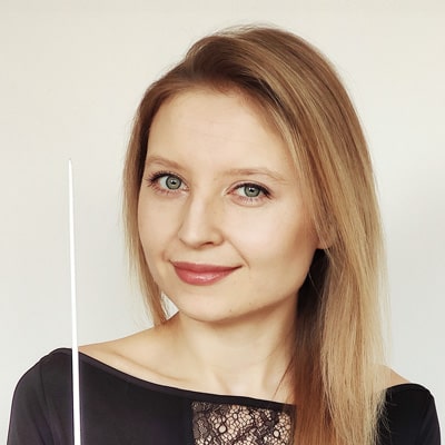 Młoda kobieta o blond włosach uśmiecha się trzymając batutę