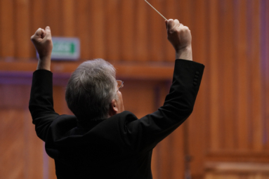 zdjęcie dyrygenta z uniesionymi ku górze rękami i zaciśniętymi pięściami