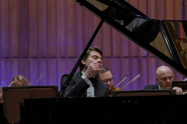 zdjęcie młodego pianisty za fortepianem, z uniesioną ręką i zamkniętymi oczai