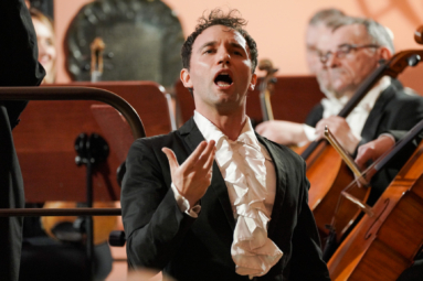 zdjęcie śpiewaka w trakcie wykonywania utworu, z ręką uniesioną ku górze