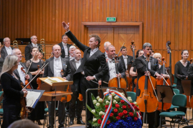 Dyrygent Paweł Kapuła wskazujący ręką na Orkiestrę Symfoniczną FP