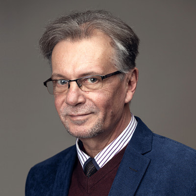 zdjęcie portretowe mężczyzny w granatowej marynarce, w okularach i rzadkich siwych włosach