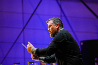 zdjęcie dyrygenta prowadzącego orkiestrę podczas koncertu plenerowego pod giwazdami