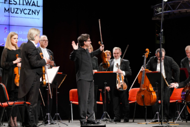 zdjęcie orkiestry stojącej na estradzie, przyjmującej oklaski publiczności