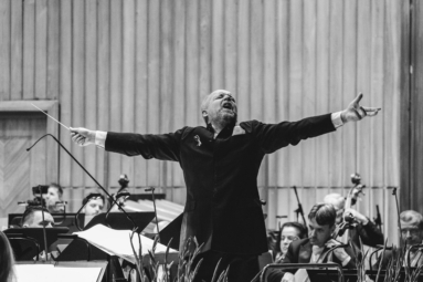 dyrygent Maciej Tworek w twórczym uniesieniu, z zamkniętymi oczami, rozłożonymi szeroko ramionami, głową zwróconą w górę