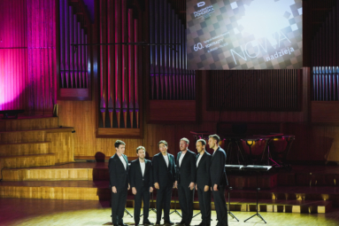 szóstka mężczyzn w czarnych garniturach stoi blisko siebie na estradzie FP, spogląda w dal i śpiewa