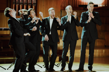 szóstka mężczyzn w czarnych garniturach. klaszcze w dłonie dobrze się przy tym bawiąc