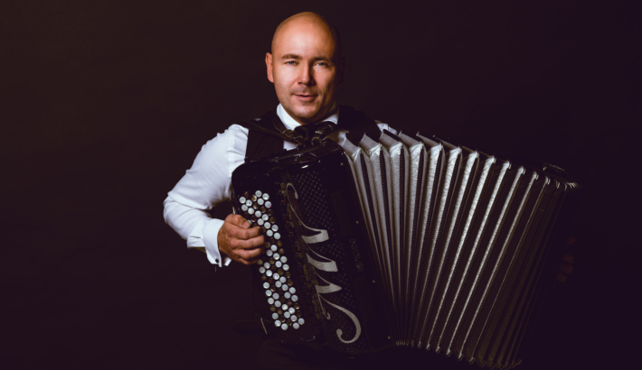 zdjęcie łysego mężczyzny trzymającego w ręku akordeon