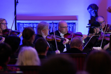 zdjęcie skrzypków Orkiestry, skupionych podczas koncertu, wpatrujących się w nuty