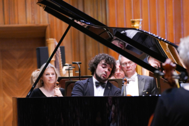 zdjęcie młodego mężczyzny w kręconych, ciemnych włosach skupionego na grze na fortepianie