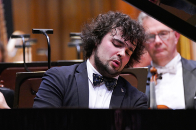 zdjęcie młodego mężczyzny w kręconych, ciemnych włosach skupionego na grze na fortepianie