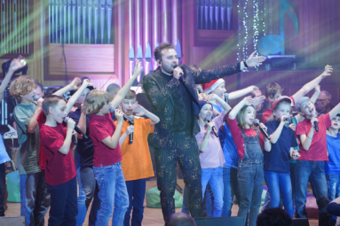 zdjęcie wokalisty i śpiewających dzieci z uniesionymi rękami