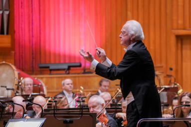 zdjęcie starszego, siwego mężczyzny, który dyryguje orkiestrą z batutą w reku