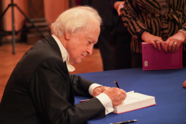 zdjęcie starszego, siwego mężczyzny podpisującego książkę