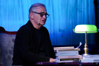 Zdjęcie aktora - Olgierda Łukaszewicza siedzącego na estradzie FP przy biurku z zapaloną zieloną lampką