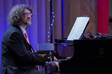 zdjęcie pianisty w długich, kręconych włosach siedzącego przy fortepianie