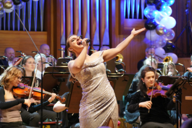 zdjęcie wokalistki w cekinowej, złotej sukience śpiewającej do mikrofonu