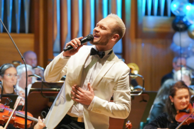 zdjęcie młodego wokalisty w białej marynarce, śpiewającego do mikrofonu