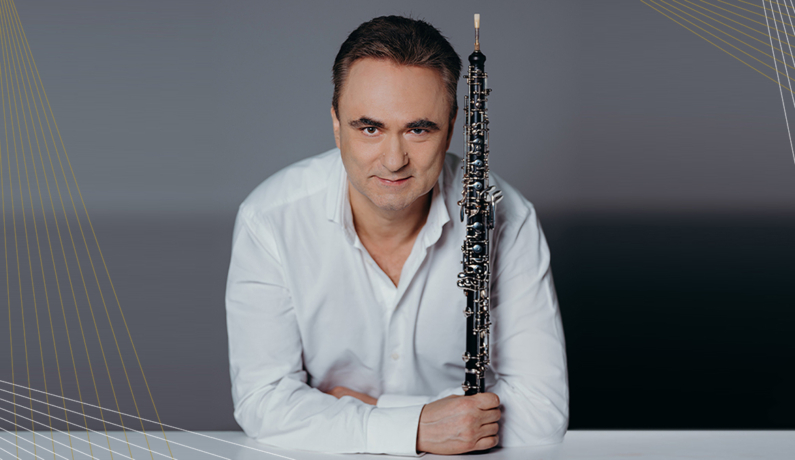 zdjęcie mężczyzny w białej koszuli opierającego się łokciami o stół, w ręku trzymającego obój