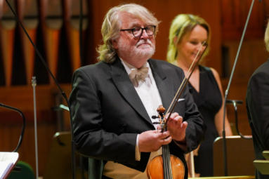 zdjęcie starszego mężczyzny o siwych, długich włosach, trzymającego w rękach skrzypce