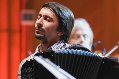 młody mężczyzna w ciemnych włosach gra na akordeonie z zamkniętymi oczami