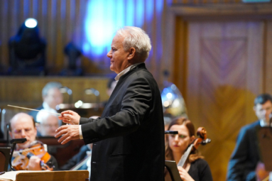 zdjęcie dyrygenta o siwych włosach spoglądającego z uśmiechem w stronę orkiestry