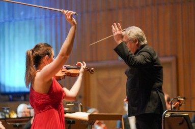 zdjęcie młodej skrzypaczki w czerwonej sukience z uniesionym wysoko smyczkiem, uchwyconej w momencie zakończenia koncertu