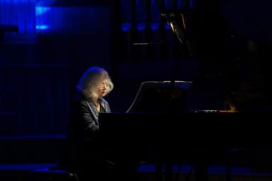 zdjęcie starszej, siwej kobiety grającej w półmroku na fortepianie