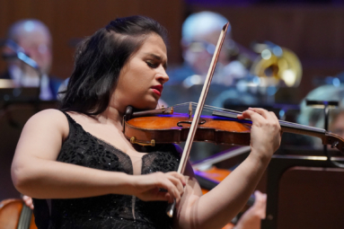 zdjęcie skrzypaczki w czarnych włosach i cekinowej sukience z odkrytymi ramionami, grającej na skrzypcach
