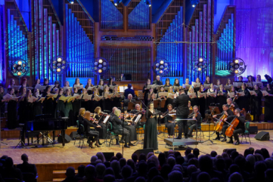 zdjęcie orkiestry kameralnej i chóru na estradzie filharmonii podświetlonej na niebiesko