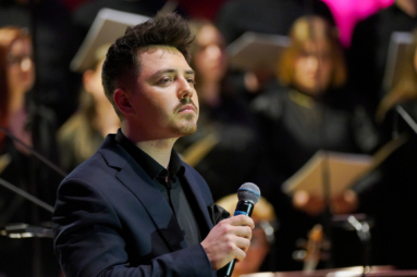 zdjęcie młodego wokalisty z poważną miną trzymającego w ręku mikrofon