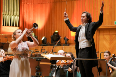 zdjęcie dyrygenta z uniesionymi rękami i solistki grającej na trąbce