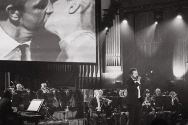 zdjęcie młodego wokalisty w garniturze i czarnej muszce z towarzyszeniem orkiestry kameralnej