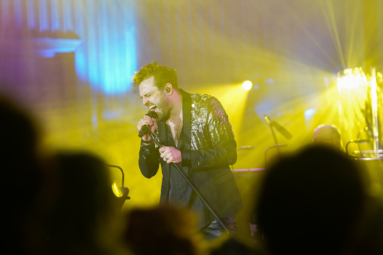 zdjęcie młodego mężczyzny w rozpiętej koszuli, śpiewającego z zamkniętymi oczami do mikrofonu