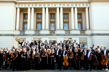 zdjęcie muzyków Orkiestry Symfonicznej FP stojących przed gmachem FP z uniesionymi ku górze instrumentami