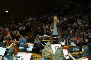 zdjęcie dyrygenta ukazanego z perspektywy orkiestry, za którym widać publiczność