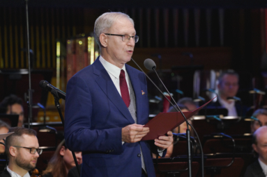 zdjęcie starszego mężczyzny w siwych włosach przemawiającego do mikrofonu