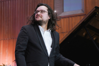 zdjęcie młodego mężczyzny w długich włosach i okularach opierającego się o fortepian