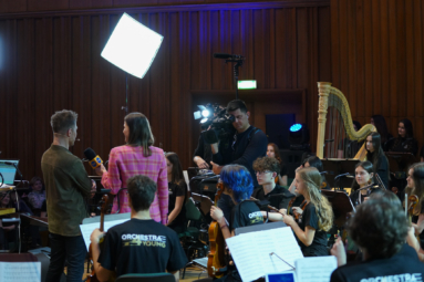 zdjęcie dziennikarki i kamerzysty w trakcie kręcenia reportażu na próbie Orchestry4Young