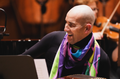 zdjęcie łysego mężczyzny w kolorowej apaszce, grającego na instrumencie