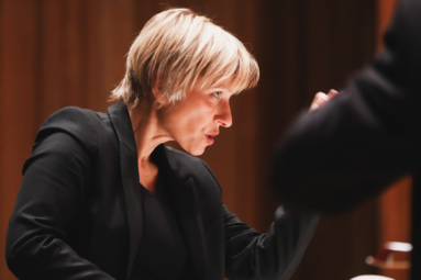 zdjęcie dyrygentki w krótkich, blond włosach patrzącej ze skupieniem w stronę orkeistry