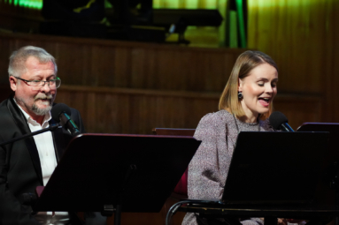 zdjęcie siwego mężczyzny z wąsem i kobiety w blond włosach siedzących za pulpitami