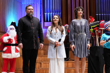 zdjęcie mężczyzny i dwóch kobiet w koncertowych strojach, zwróconych w stronę publiczności