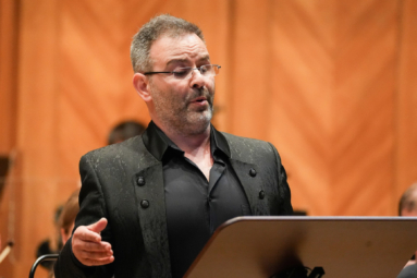 mężczyzna w okularach spoglądający na puplit i śpiewający