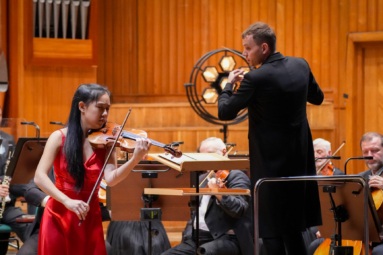 młoda skrzypaczka w czerwonej sukience i młody dyrygent we fraku podczas koncertu symfonicznego