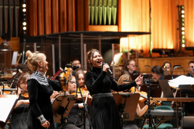 zdjęcie dwóch młodych wokalistek śpiewających z towarzyszeniem orkeistry
